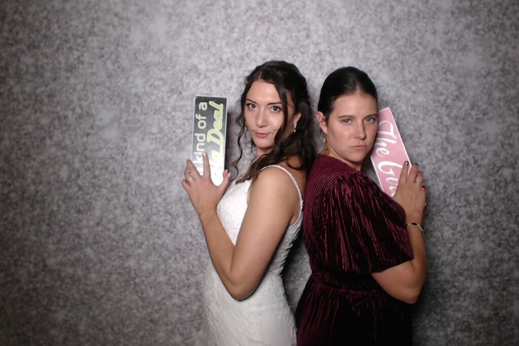 Two people posing back to back holding sign props in the photo booth